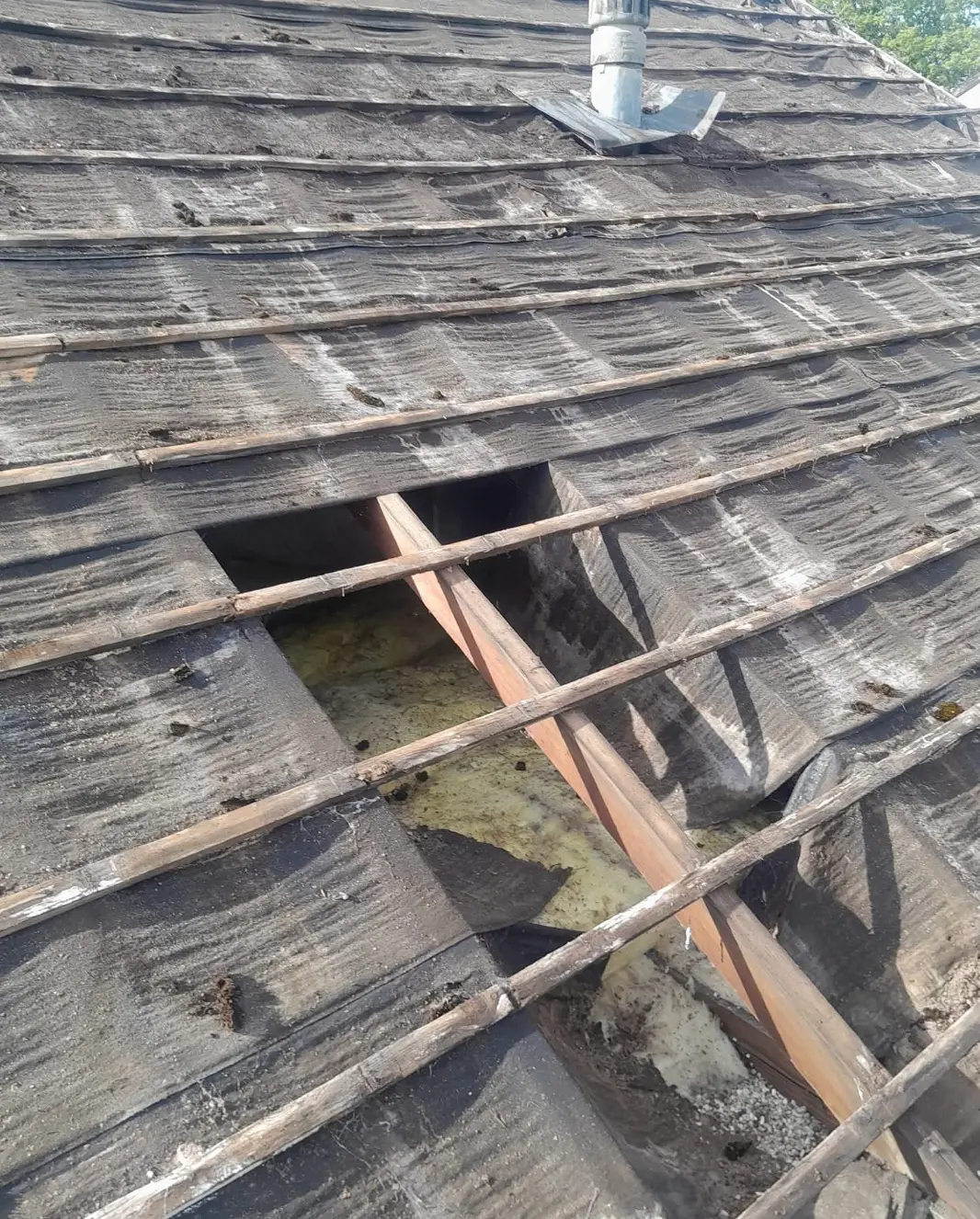 Old roof stripped back showing perished felt, broken battens and a hole through to the insulation